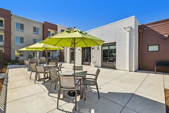 our patio has tables and chairs with umbrellas and a building in the background